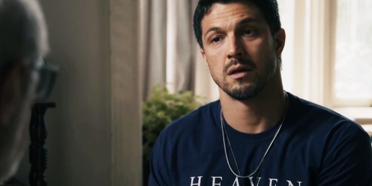 Oto em cena da novela Travessia surpreso usando camiseta azul escura e uma corrente de prata Oto em cena da novela Travessia surpreso usando camiseta azul escura e uma corrente de prata