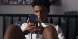 Theo sentado na cama segurando celular em cena da novela Travessia Theo sentado na cama segurando celular em cena da novela Travessia